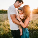 Nanda & Associate Lawyers Canada - Husband and wife hugging and holding baby outside in a grass field